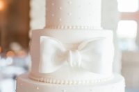 a white wedding cake with plain and polka dot tiers, with neutral blooms on top and a white sugar bow is a chic and elegant idea to rock