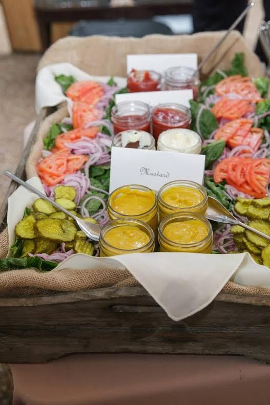 a wooden tray with burlap, with pickled onions, tomatoes, cucumbers, greenery and various sauces