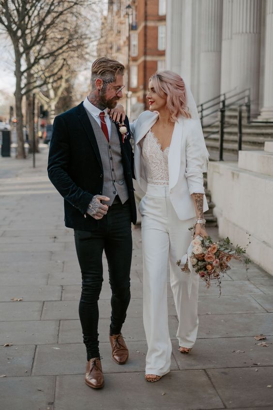 an elegant groom's look with black skinnies, a white shirt, a red tie, a grey waistcoat and a navy velvet blazer, head and hand tattoos