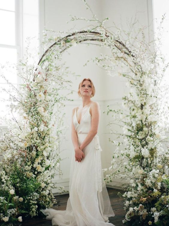 an ethereal wedding arch with greenery and white blooms and blooming branches all around is amazing