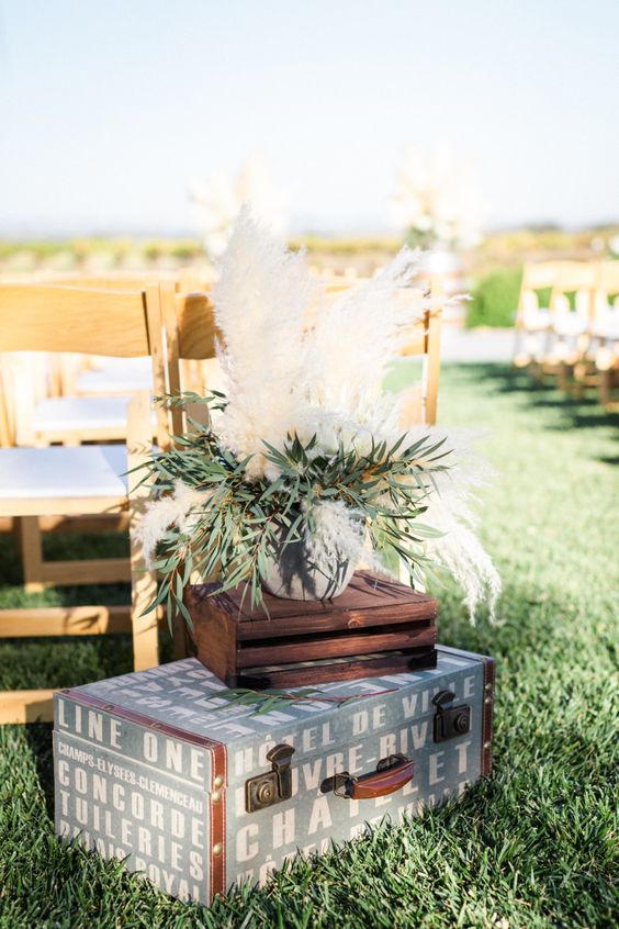 wedding ceremony space decor with a wooden crate, a vintage suitcase, an arrangement of greenery and pampas grass