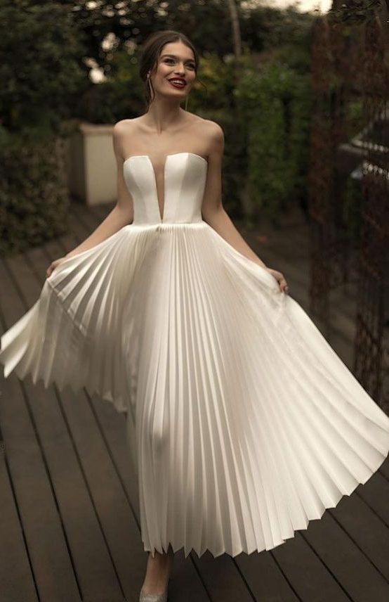 an exquisite A-line wedding dress with a corset bodice with a plunging neckline and a pleated midi skirt is an out of the box idea