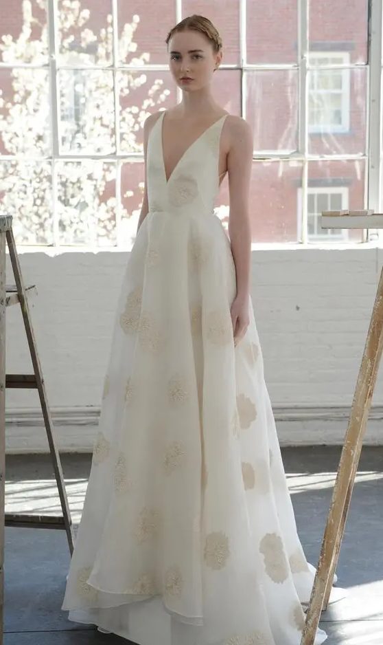 an A-line white wedding dress with gold lace applique, no sleeves and a plunging neckline that is that sexy detail that will catch an eye
