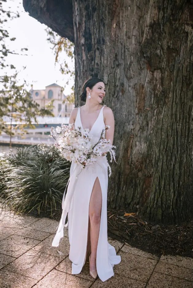a modern glam bride wearing a plain A-line wedding dress with no sleeves, a deep neckline and a front slit, nude shoes and statement earrings