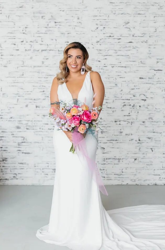 a minimalist mermaid wedding dress with a covered plunging neckline and statement earrings and a train