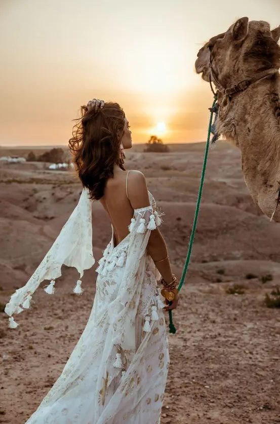 a boho A-line wedding dress in white, with gold lace detailing, tassels, a low back and a cold shoulder is very refined and chic
