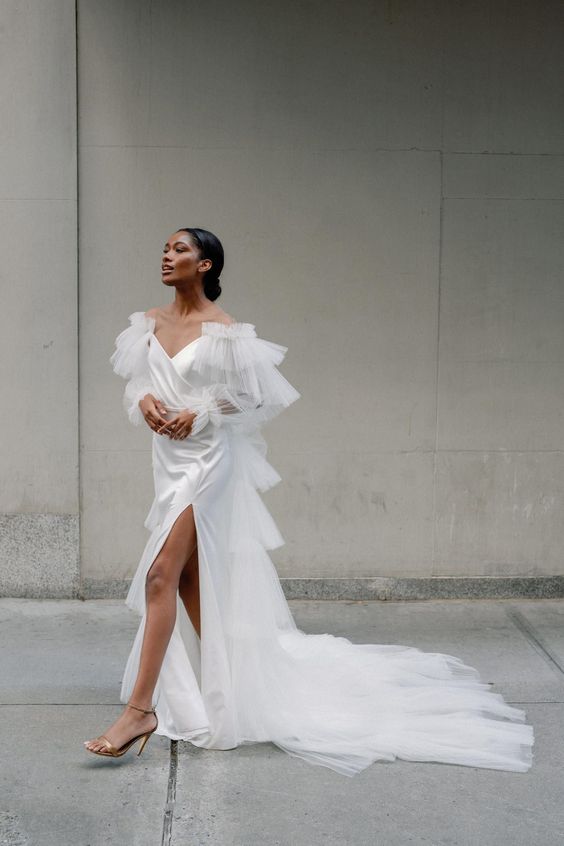 an unusual and sophisticated off the shoulder wedding dress with a draped bodice, ruffles all over, a long train and a thigh high slit for a sexy touch