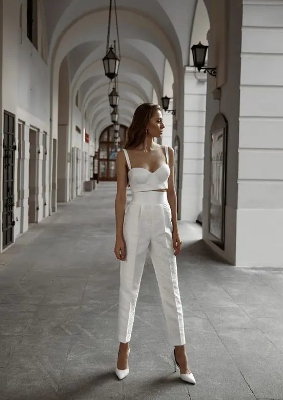 a sexy bridal look with a corset-like crop top and high waisted cropped trousers, white heels and pearl earrings