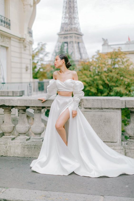 an exquisite and romantic bridal look with an off the shoulder crop top with a draped bodice, an A-line skirt with thigh high slit and a train