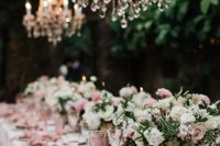 a beautiful garden wedding tablescape with white and blush blooms and greenery, pink linens, pink glasses and crystal chandeliers