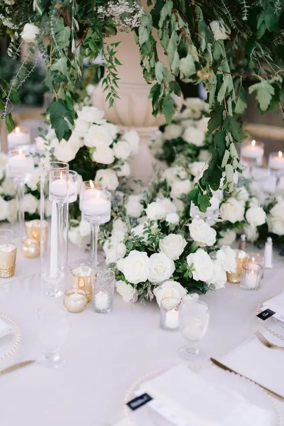 a beautiful secret garden wedding table setting in white, with roses, candles, elegant neutral linens and a lush greenery centerpiece