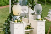a beautiful vintage drink bar of a vintage vanity, with drawers and lemonade on stands, with greenery and citrus is a veyr cool idea
