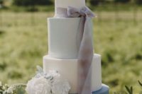 a beautiful white, light blue and navy wedding cake with lace detailing, a grey ribbon bow and white blooms for a spring wedding