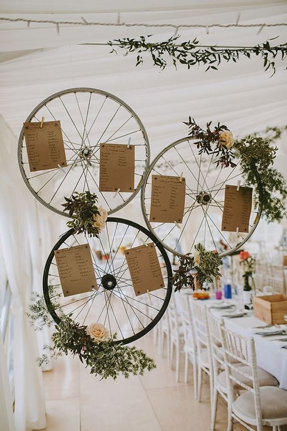 a bike wheel seating plan with greenery, neutral blooms and the plan itself is a stylish and cool idea for a wedding