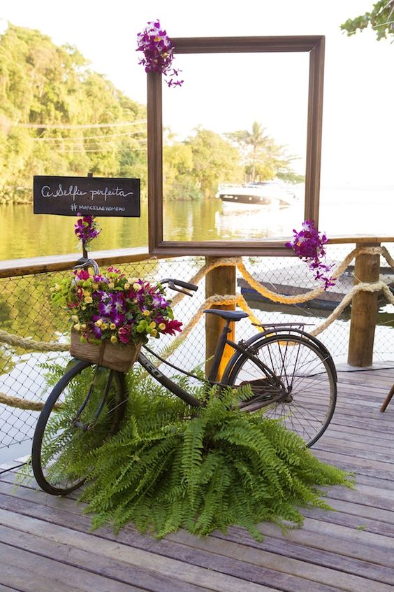 a black bike decorated with ferns and with a basket filled with super bright blooms and greenery is a gorgeous idea for a wedding