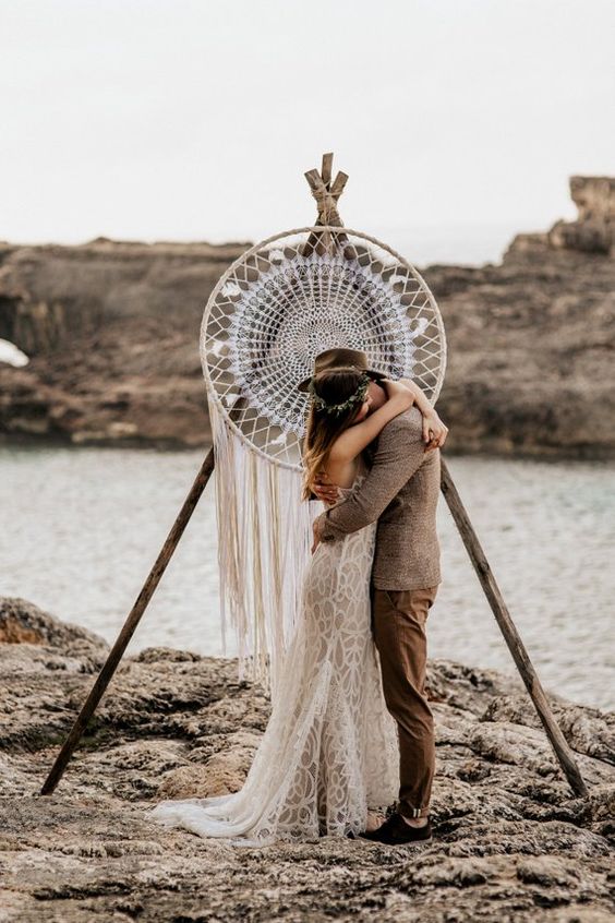 A boho wedding arch with a large dream catcher with fringe is a cool idea for any boho couple