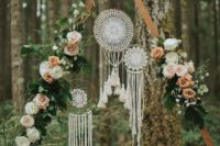 a boho wedding arch with greenery, blush and pastel blooms and some dream catchers hanging inside