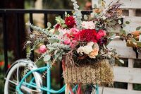 a bright turquoise bike with a wire basket, bold pink, red and neutral blooms and greenery is a fun and cool decor idea for a wedding