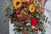 a cascading fall wedding bouquet of sunflowers, yellow roses, red dahlias, berries, greenery and seed pods is a lovely idea for a bold wedding