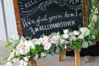 a catchy chalkboard wedding sign with chalking, white, blush blooms and greenery will be a perfect fit for a rustic wedding
