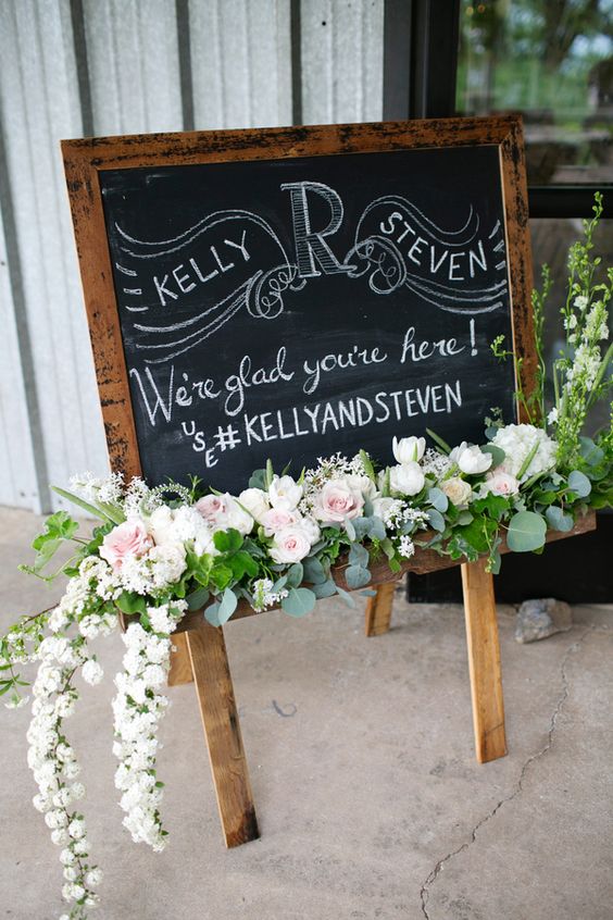 a catchy chalkboard wedding sign with chalking, white, blush blooms and greenery will be a perfect fit for a rustic wedding