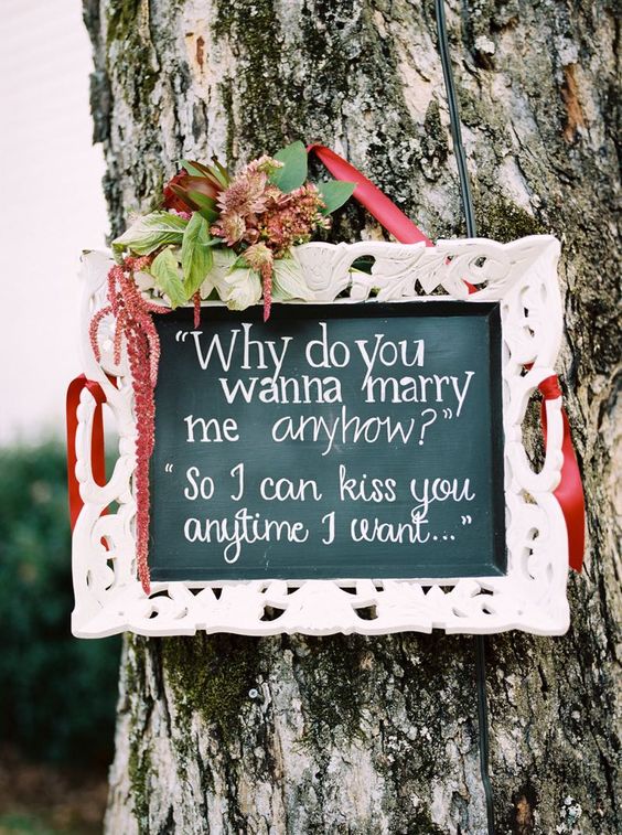 a chalkboard sign in a refined white frame, with burgundy blooms, greenery and ribbon is a lovely idea for a wedding in the fall