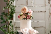 a chic and exquisite whie wedding cake with patterns, a white ribbon bow and pink and neutral florals on top for a garden wedding