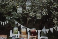 a chic and relaxed wedding drink bar of a green sideboard, crates with lemonade, cages on the trees and buntings is amazing