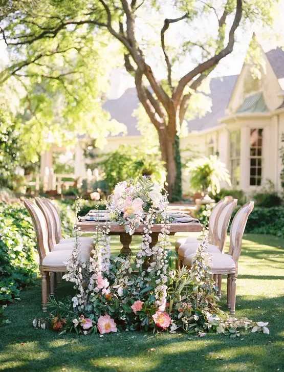 a chic garden wedding table setting with neutral and pastel blooms, with greenery on the ground and on the table