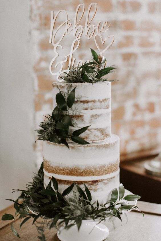 a chic naked wedding cake with greenery, thistles, a chic gold topper for a modern wedding