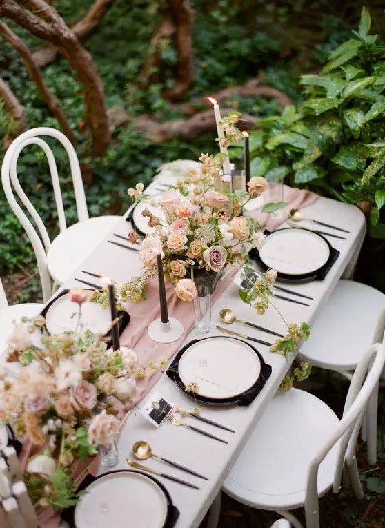 a chic secret garden wedding table setting with a pink runner, black candles, napkins and blush blooms and greenery