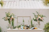 a chic wedding bar of a white bar stand, greenery and pastel floral arrangements, an open shelf is a lovely idea