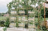 a chic wedding drink bar with gilded stands with drinks and lots of greenery garlands and white blooms is a beautiful idea