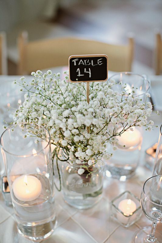 a delicate cluster wedding centerpiece of baby's breath, floating and pillar candles and a chalkboard table number is a lovely idea for a wedding