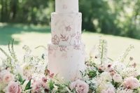 a delicate garden wedding cake with pink and mauve blooms painted and lush blooms around is amazing