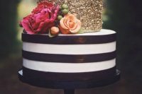 a glam wedding cake with a striped black and white tier and a gold glitter one, with orange and fuchsia blooms and a gold glitter topper