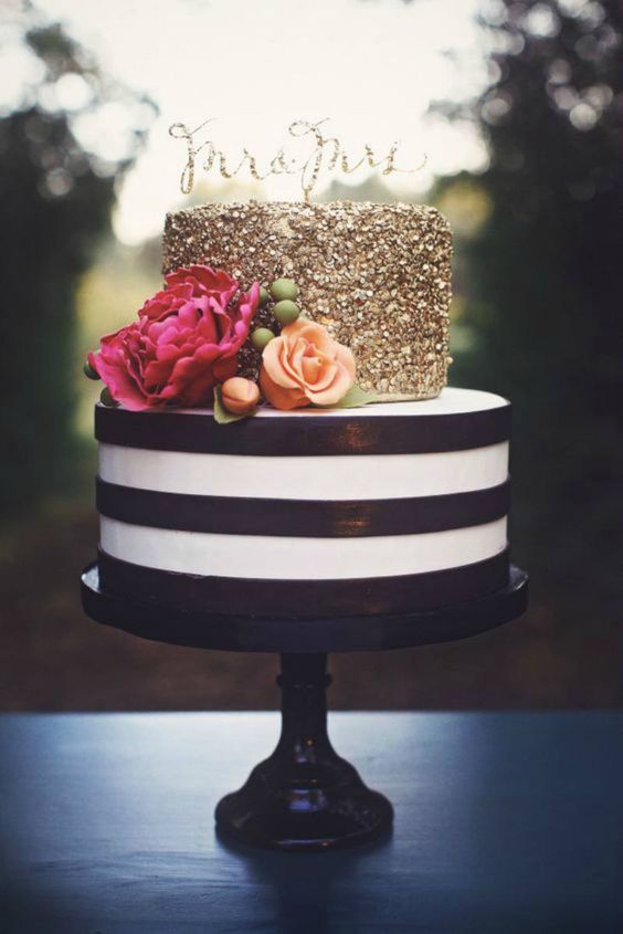 a glam wedding cake with a striped black and white tier and a gold glitter one, with orange and fuchsia blooms and a gold glitter topper