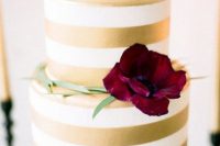 a gold and white striped wedding cake with greenery and a burgundy bloom is a chic and stylish idea for many weddings