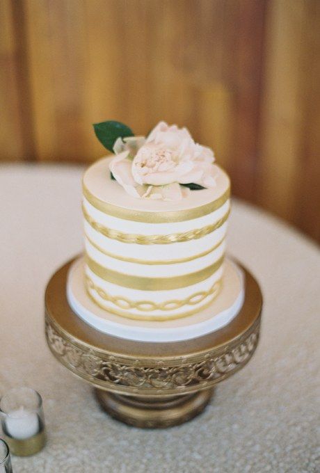 a gold and white wedding cake with a white bloom on top is a chic idea for a modern spring or summer wedding with a touch of gold