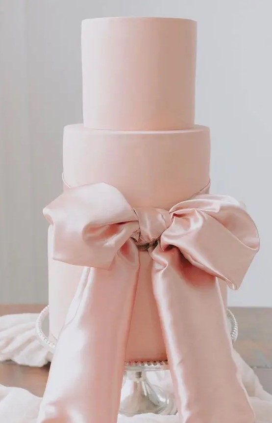 a large pink wedding cake with a large pink silk bow of ribbon is a gorgeous idea for a refined wedding done with pastel colors