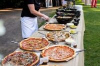 a long wedding pizza table with pizzas on metal trays that warm up the food and dips and sauces