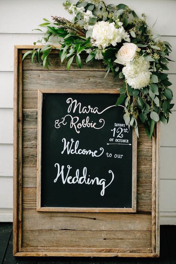 a lovely wedding sign of reclaimed wood, a chalkboard sign, some white blooms and greenery is a gorgeous idea for a rustic wedding