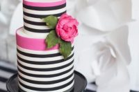 a modern black and white wedding cake with hot pink touches and a hot pink bloom with greenery is a lovely and glam idea