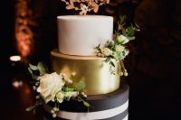 a modern wedding cake with a black and white striped tier, a gold one and a white one, with white blooms and a calligraphy topper