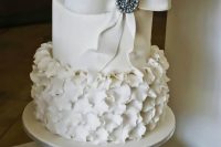 a neutral wedding cake with plain and petal tiers, with a large sugar bow and a brooch is a chic and stylish wedding dessert with a vintage feel