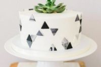 a one tier wedding cake decorated with grey and black and marbleized triangles and a succulent on top