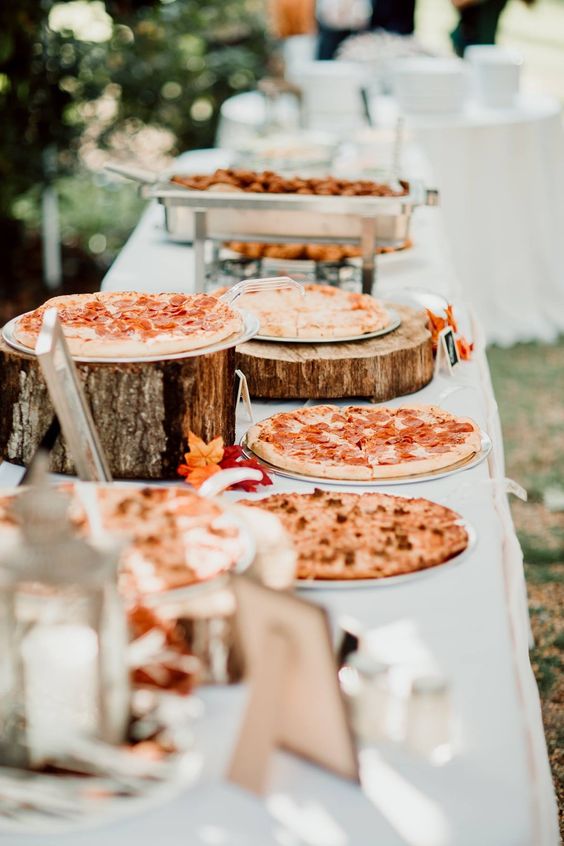 a pizza bar with pizzas on tree stumps and slices or on plates plus condiments and other food
