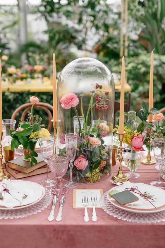 a pretty garden wedding centerpiece of a cloche with pink and yellow blooms and greenery, floral arrangements on book stacks