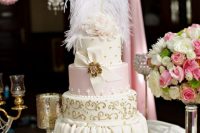a refined Marie Antoinette wedding cake in pink, ivory and gold, with patterns, beads and a sugar bow with a gold brooch and feathers