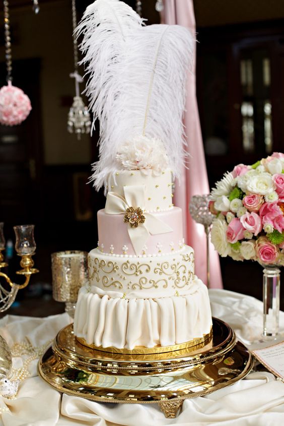 a refined Marie Antoinette wedding cake in pink, ivory and gold, with patterns, beads and a sugar bow with a gold brooch and feathers